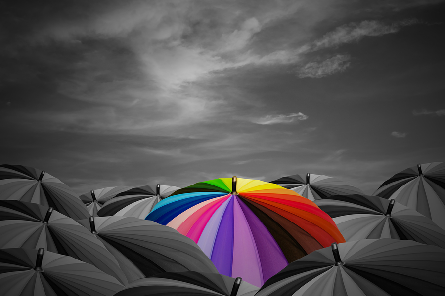 Rainbow umbrella are in a black umbrellas on storm sky background